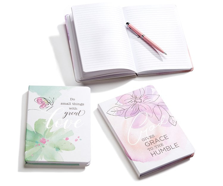 Two  journal notebooks  show the pretty covers.  There is a third that is laying open with a pen laying across it.  Green flower & butterfly design  “Do small things with Great Love”.   Pink with flower design “God gives grace to the humble”.  6561154826404