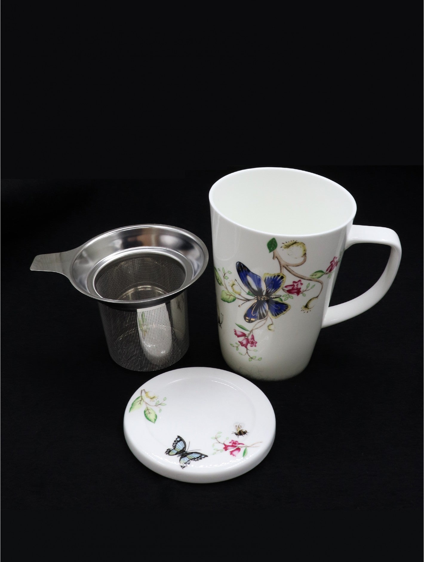 White tea mug with a picture of a butterfly on a red flower vine.  Laying beside it is an infuser that fits in the mug and the lid.  The lid is decorated with small images of a small butterfly and flowers.