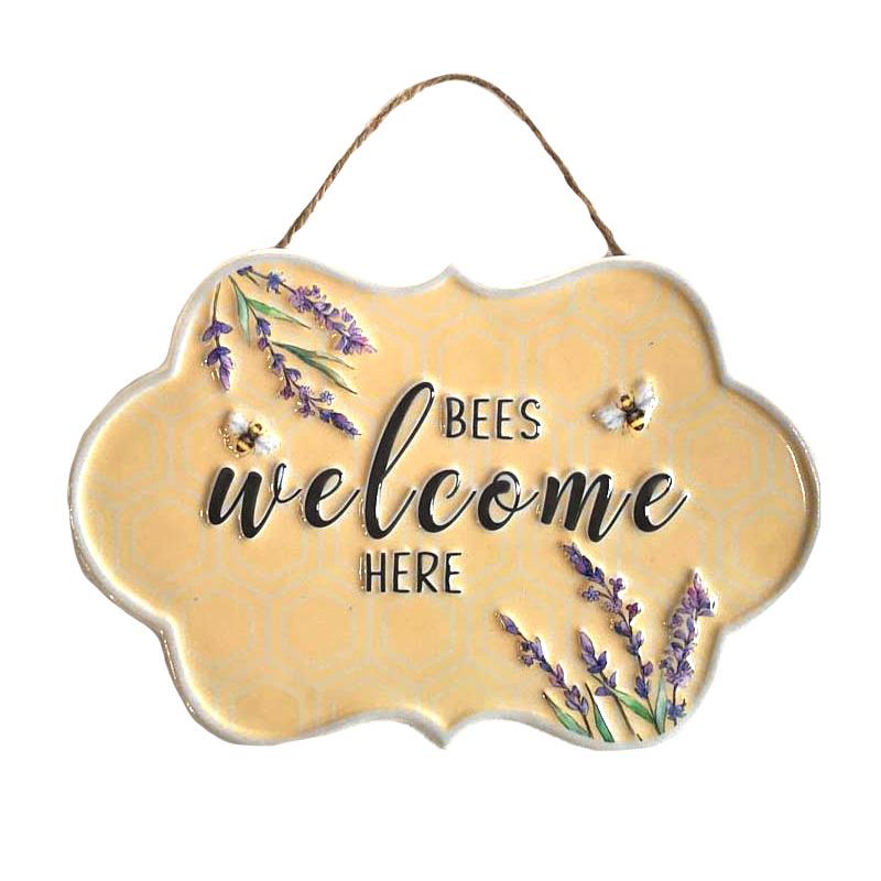 Yellow plaque with printed lavender flowers, black typography that says Bees Welcome Here hung from a sisal cord